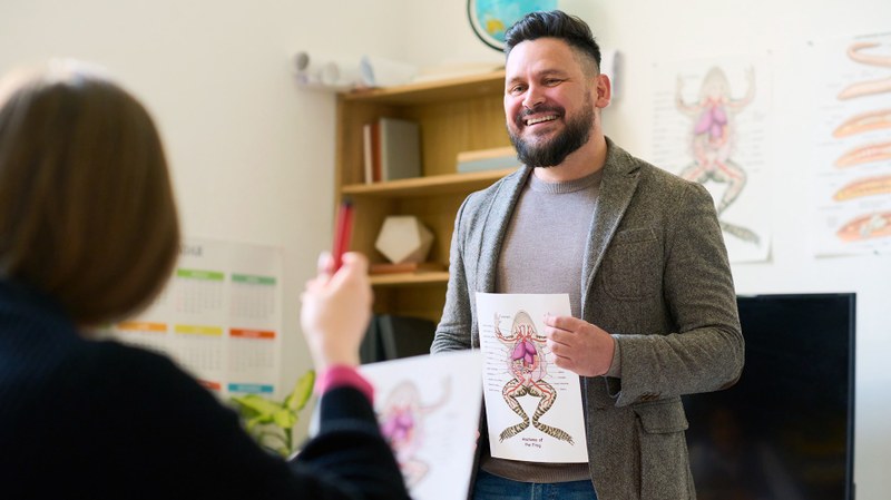 Lehrer steht vor der Klasse und zeigt ein Aufgabenblatt zur Anatomie des Frosches in der Hand