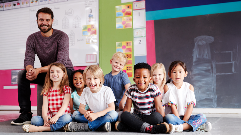 Ein Lehrer sitzt gut gelaunt mit seiner multiethnischen Klasse im Klassenzimmer