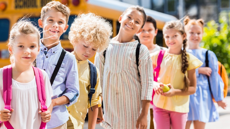 Schulkinder stehen in einer Reihe hintereinander vor einem gelbem Schulbus