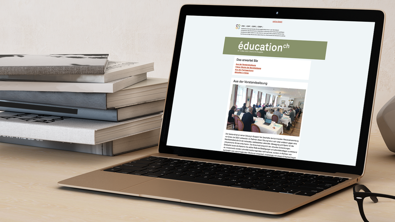 Aufgeklappter Laptop, auf dem Bildschirm ist der EDK-Newsletter zu sehen, links neben dem Laptop ein Stapel Bücher.