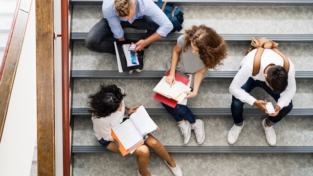 Group of young students sitting on the school building stairs