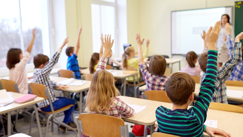 Groupe d'écoliers levant la main dans la salle de classe
