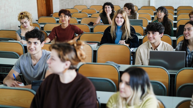 Des étudiants écoutent attentivement et souriants dans un amphithéâtre de l'université.